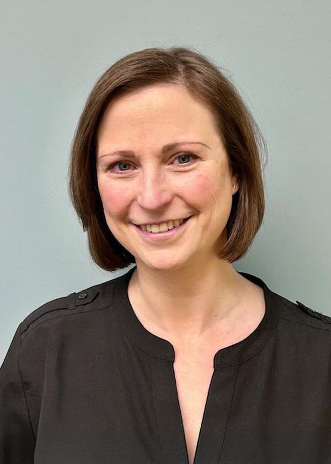 Against a plain light-colored background, Dr. Brandy McGee, with short brown hair and a smile, is wearing a black top.