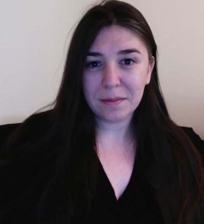 A person with long dark hair and a neutral expression, resembling someone seeking anxiety treatment, is wearing a dark top against a plain light background, possibly in the office of Dr. Melisa Robichaud or another psychologist.