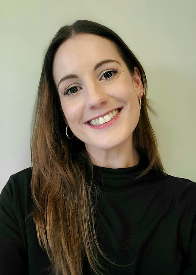 A smiling Dr. Rachael Neal, with long brown hair and hoop earrings, poses elegantly in a black top against a plain background.